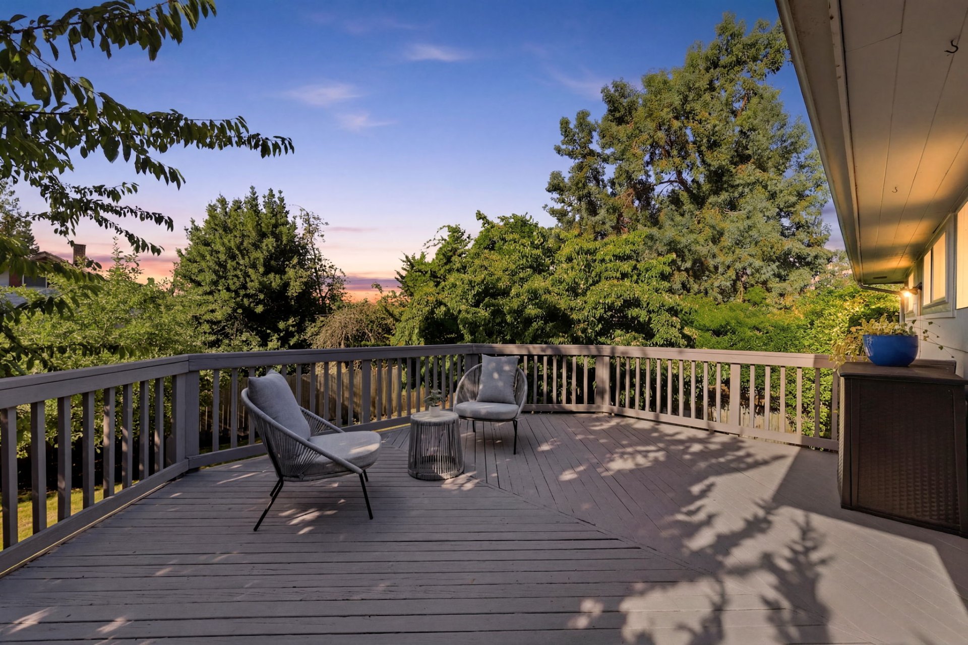 Backyard deck at sunset with two outdoor chairs, a small table, and tree-lined views